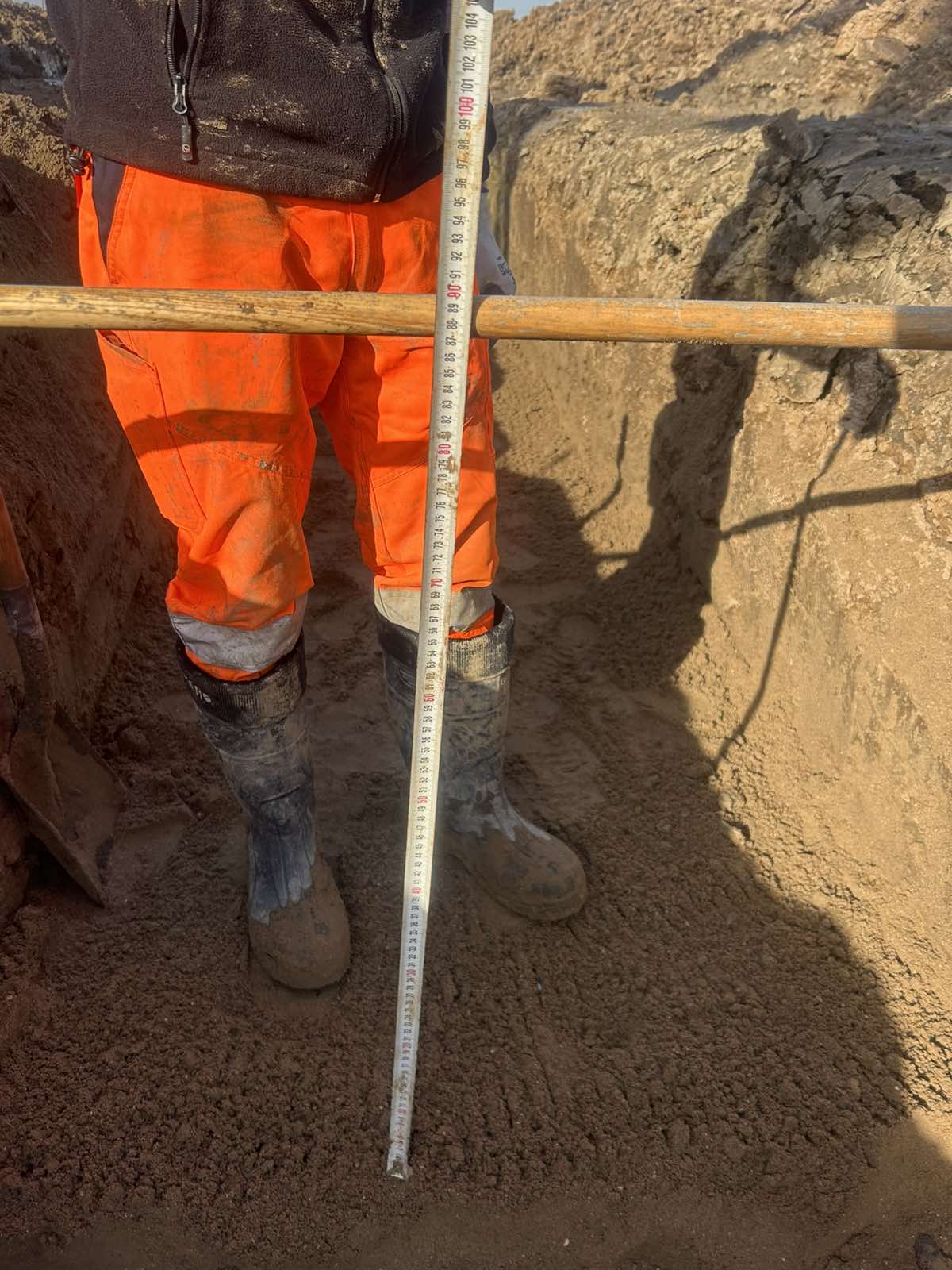 Worker measuring depth in trench with ruler.
