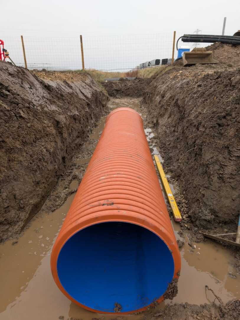 Orange drainage pipe in muddy trench installation.